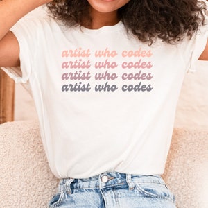 May include: A white t-shirt with the text "artist who codes" repeated four times in a gradient of pink, peach, and gray.