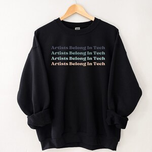 May include: Black sweatshirt with the text "Artists Belong In Tech" repeated four times in a gradient of colors, starting with dark blue and fading to light peach.