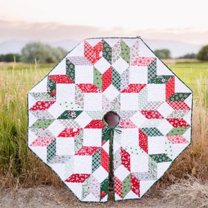Pode incluir: Uma saia de árvore de Natal com um design de estrela. A saia apresenta um padrão de retalhos de tecidos vermelhos, verdes e brancos. A saia tem uma forma circular com uma fenda para o tronco da árvore e uma borda verde.