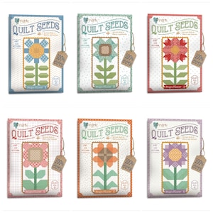 May include: Six colorful quilt seed packets featuring flower designs. Each packet has a different color scheme, including blue, green, red, pink, orange, and purple. The packets have the text "QUILT SEEDS" and "100% CUTE" on them.