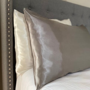May include: A grey satin pillowcase on a grey headboard with a white pillowcase underneath.