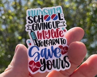 May include: A white sticker with the text "Nursing School: Giving Up My Life To Learn To Save Yours" in red, blue, and black lettering. The sticker features a red heart with a heartbeat line, a blue pill, and a syringe.