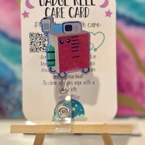 May include: A badge reel with a cute medical machine design. The badge reel has a red, blue, and green color scheme with glitter accents. The card reads "BADGE REEL CARE CARD" and includes care instructions.