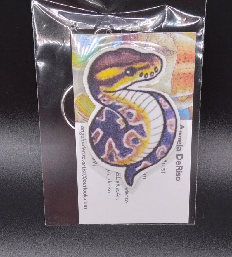 May include: A colorful keychain featuring a snake with a blue and yellow pattern. The keychain is made of wood and has a metal ring for attaching to keys.