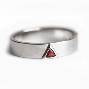 May include: A silver band ring with a triangular red gemstone set in the center.