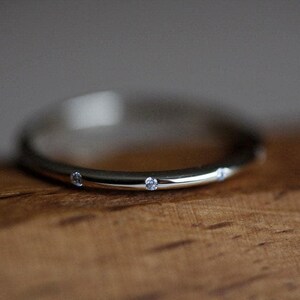 May include: A thin silver band with four small diamonds set into the metal.