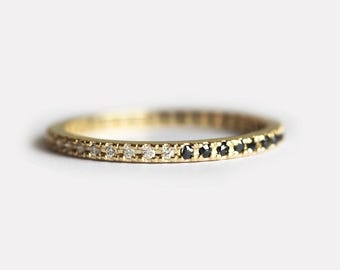 May include: A gold band ring with a row of small white diamonds and a row of small black diamonds.