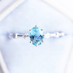 May include: A silver ring with a large oval blue aquamarine gemstone surrounded by smaller clear gemstones.