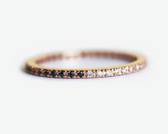 May include: A delicate rose gold band ring with a row of alternating black and white diamonds.