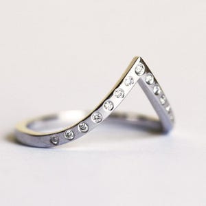 May include: A silver ring with a V-shaped design and small diamonds set along the band.
