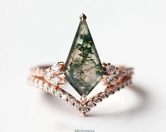 May include: A rose gold ring with a unique, geometric design. The ring features a central, clear, diamond-shaped stone with green inclusions, resembling a landscape. The band is adorned with small, sparkling diamonds, creating a delicate and elegant look.