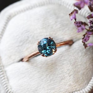 May include: A delicate rose gold ring with a deep blue oval gemstone set in a prong setting.