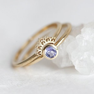 May include: A delicate gold ring set with a small, round, purple gemstone. The ring features a delicate, intricate design around the gemstone.