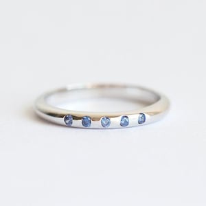 May include: A silver band ring with five small blue sapphires set in a row.