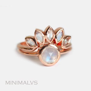 May include: A rose gold ring with a large round moonstone center stone and five smaller marquise-shaped moonstones set in a row above the center stone.