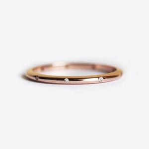 Può includere: Un sottile anello a fascia in oro rosa con tre piccoli diamanti incastonati nella fascia.