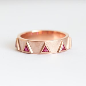 May include: A rose gold band ring with a brushed finish and triangular accents set with pink gemstones.