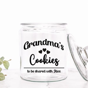 May include: A clear glass cookie jar with a lid. The jar has a black vinyl sticker that says "Grandma's Cookies to be shared with Alex".