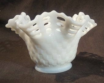 May include: A white milk glass bowl with a ruffled, openwork rim. The bowl has a woven pattern and a smooth, rounded base.