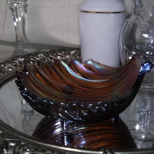 May include: A iridescent glass bowl with a scalloped edge and a wavy design. The bowl is sitting on a silver tray with a mirrored surface.