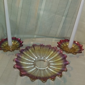 May include: A set of three iridescent glass candle holders with a scalloped edge. The holders are in shades of pink, yellow, and gold. Two of the holders have white candles.