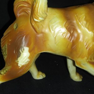 May include: A ceramic figurine of a brown and white dog with a long tail. The dog is standing on all four legs and has a slightly tilted head.