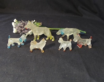 May include: A collection of six clear plastic dog figurines. The dogs are in various poses and sizes, and some have painted details in blue, red, and yellow.