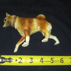 May include: A brown and white plastic toy dog figurine. The dog is in a running pose with its head turned to the left. The dog is about 15 cm long.