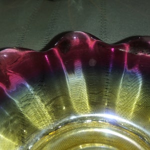 May include: A glass bowl with a scalloped edge. The bowl is iridescent with shades of pink, blue, and yellow.