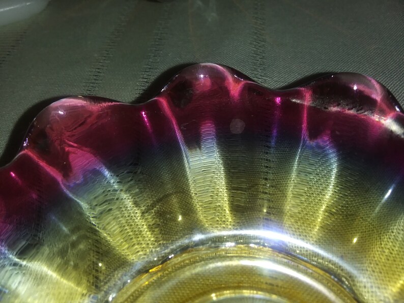 May include: A glass bowl with a scalloped edge. The bowl is iridescent with shades of pink, blue, and yellow.