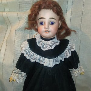 May include: Antique porcelain doll with blue eyes and a black velvet dress trimmed with white lace.