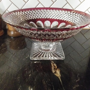 May include: A clear glass bowl with a red rim and intricate cut glass design. The bowl sits on a square pedestal with a cut glass design.