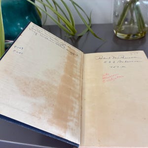 May include: An open book with aged, cream-colored pages. Handwritten text and signatures are visible on the pages. The book has a dark blue cover. The book is slightly open, revealing the interior pages.