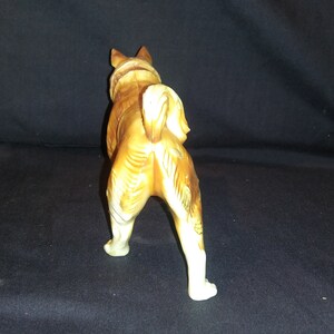 May include: A ceramic figurine of a brown and white dog standing on all four legs. The dog is facing away from the camera and has its tail curled up.