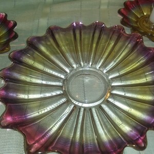 May include: A set of three iridescent glass candle holders with a scalloped design. The holders are in shades of pink, yellow, and gold.