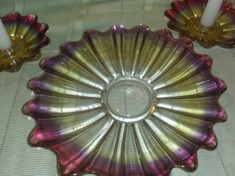 May include: A set of three iridescent glass candle holders with a scalloped design. The holders are in shades of pink, yellow, and gold.