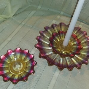 May include: Two iridescent glass candle holders shaped like flowers. The larger holder has a white candle in it. The smaller holder is empty.