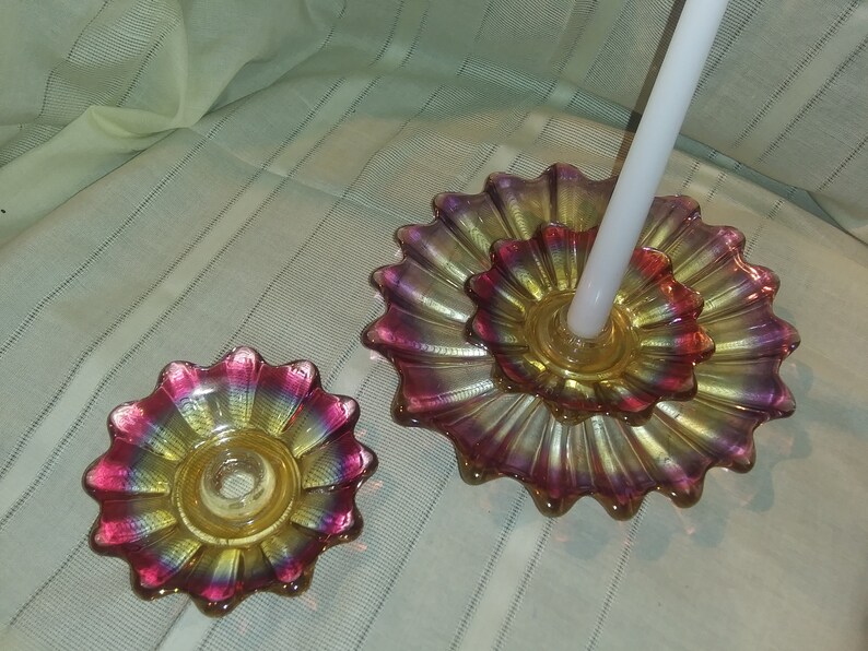 May include: Two iridescent glass candle holders shaped like flowers. The larger holder has a white candle in it. The smaller holder is empty.