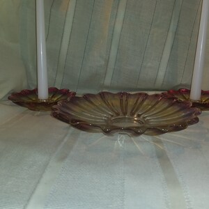 May include: Two white candles in glass candle holders with a scalloped, iridescent pink and yellow glass dish.