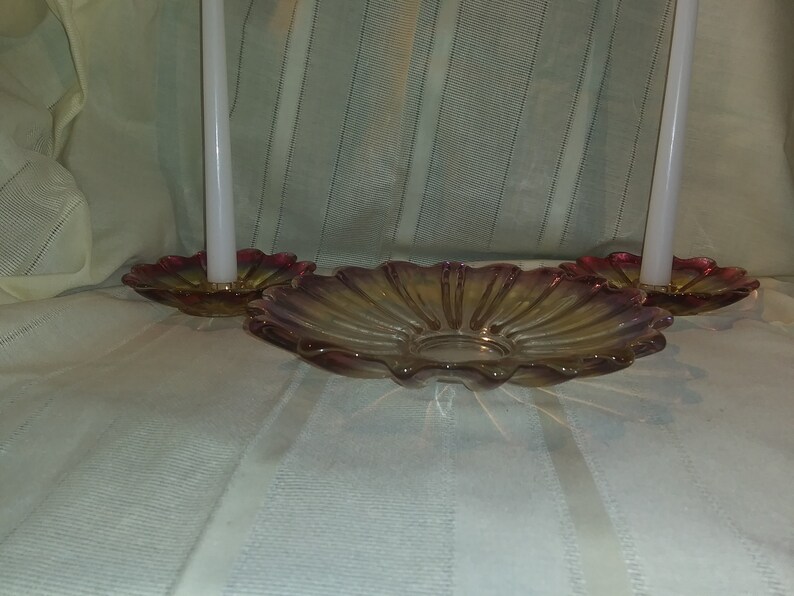 May include: Two white candles in glass candle holders with a scalloped, iridescent pink and yellow glass dish.