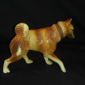 May include: A ceramic figurine of a brown and white dog with a brown leather collar. The dog is standing on all four legs and has its head turned to the side.