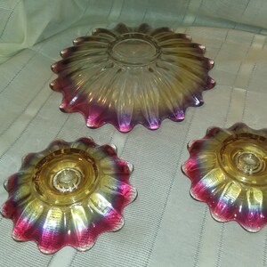 May include: Set of three iridescent glass dishes with a scalloped edge. The dishes are yellow, pink, and purple with a gold iridescent finish. The largest dish is a serving bowl, and the two smaller dishes are candle holders.