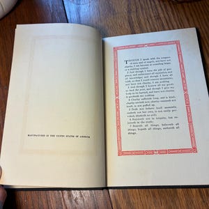 May include: Open book with English text, a decorative red border on the right page, and the text "MANUFACTURED IN THE UNITED STATES OF AMERICA" on the left. The book is open on a wooden surface.