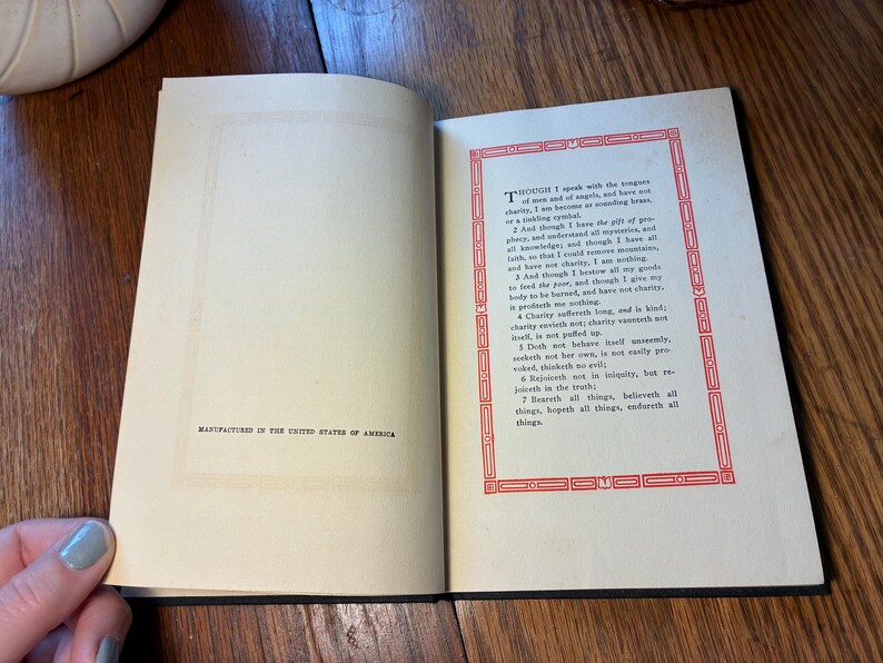 May include: Open book with English text, a decorative red border on the right page, and the text "MANUFACTURED IN THE UNITED STATES OF AMERICA" on the left. The book is open on a wooden surface.