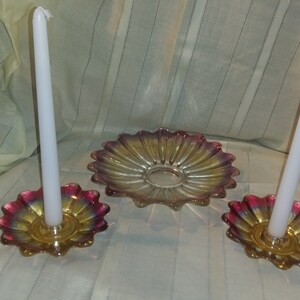 May include: A set of three iridescent glass candle holders. The holders are shaped like flowers with a central ring for holding a candle. The centre holder is larger and has a flat surface for holding a decorative item.