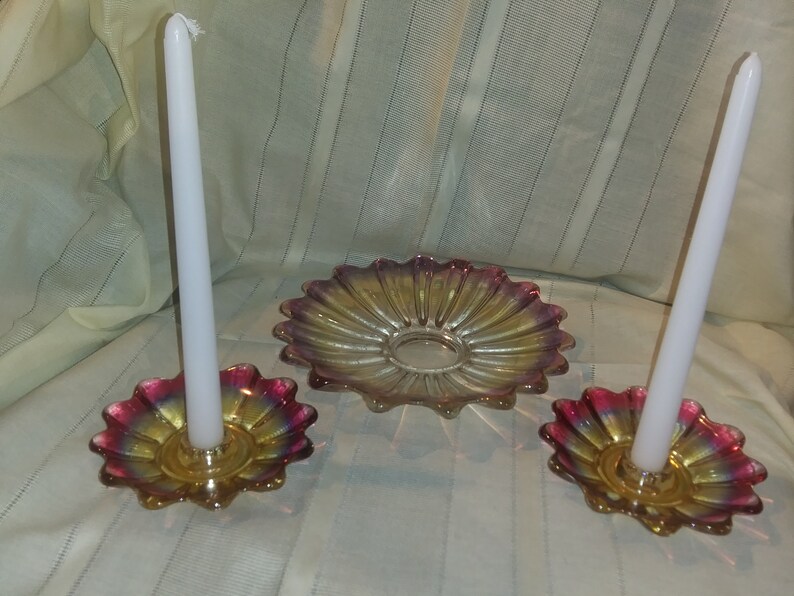 May include: A set of three iridescent glass candle holders. The holders are shaped like flowers with a central ring for holding a candle. The centre holder is larger and has a flat surface for holding a decorative item.