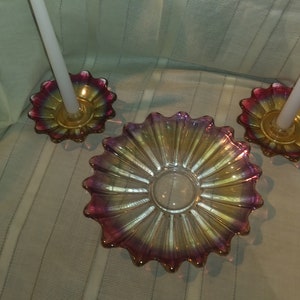 May include: A set of three iridescent glass candle holders with a pink and gold colour scheme. The holders are shaped like a flower with a central well for a candle.