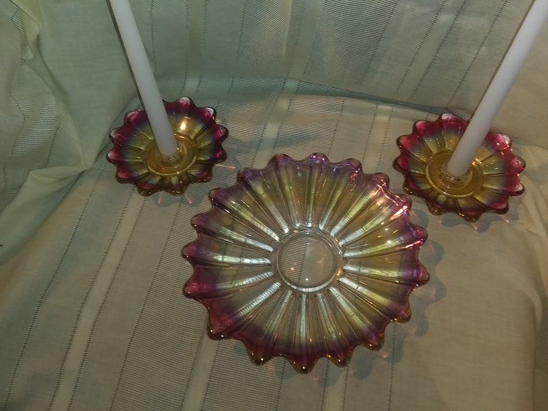May include: A set of three iridescent glass candle holders with a pink and gold colour scheme. The holders are shaped like a flower with a central well for a candle.