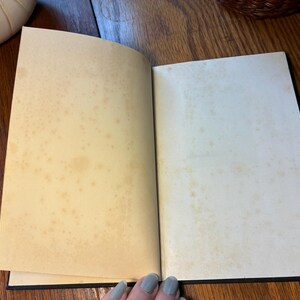 May include: An open book with aged, yellowed pages. The pages have brown spots and stains, suggesting age or use. The book's binding is black, and the pages are slightly curved. The book is on a wooden surface.