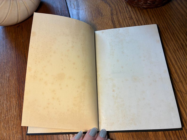 May include: An open book with aged, yellowed pages. The pages have brown spots and stains, suggesting age or use. The book's binding is black, and the pages are slightly curved. The book is on a wooden surface.